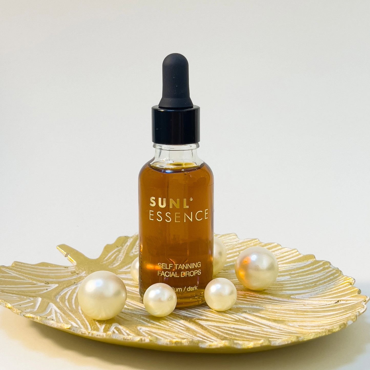 Gotas Autobronceadoras Sunl’essence sobre bandeja decorativa dorada con perlas