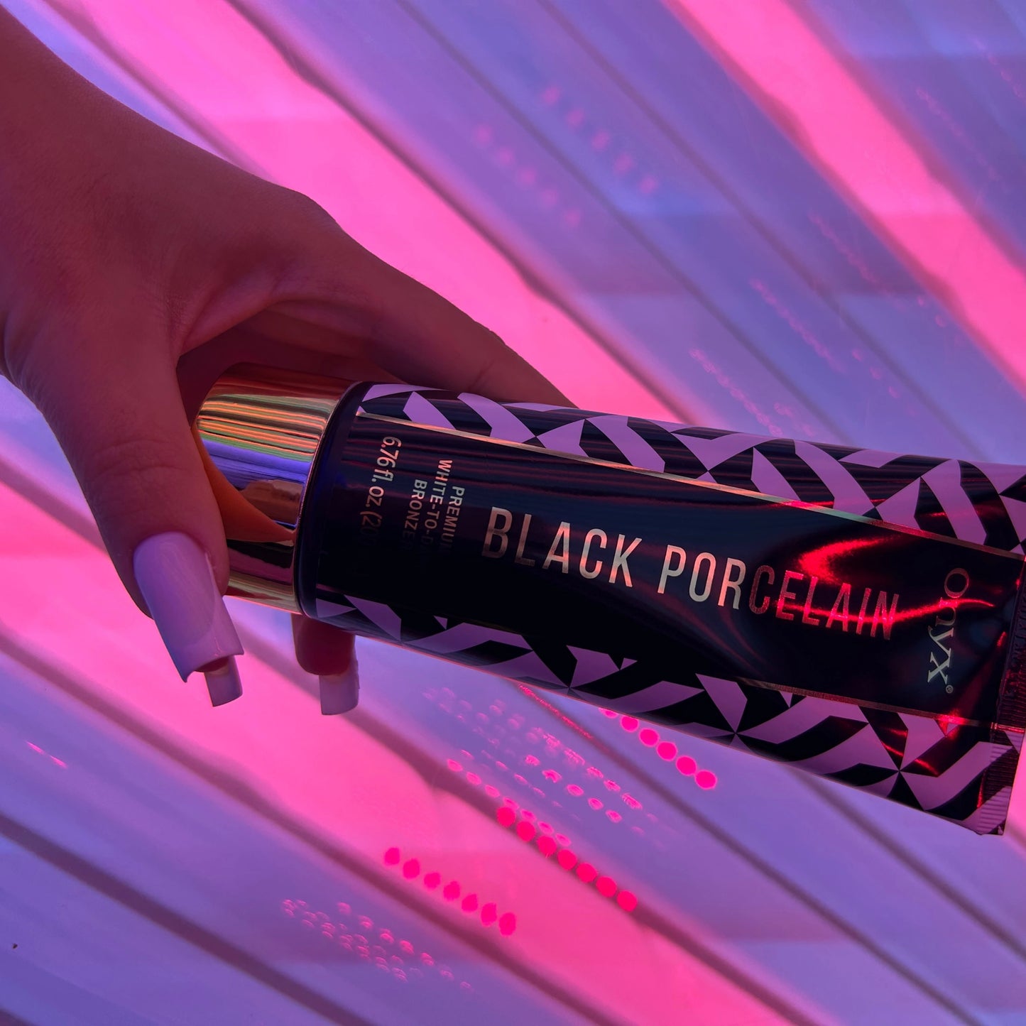 La loción bronceadora Onyx Black Porcelain reposa en una mano con uñas largas frente a luz rosa en el solarium