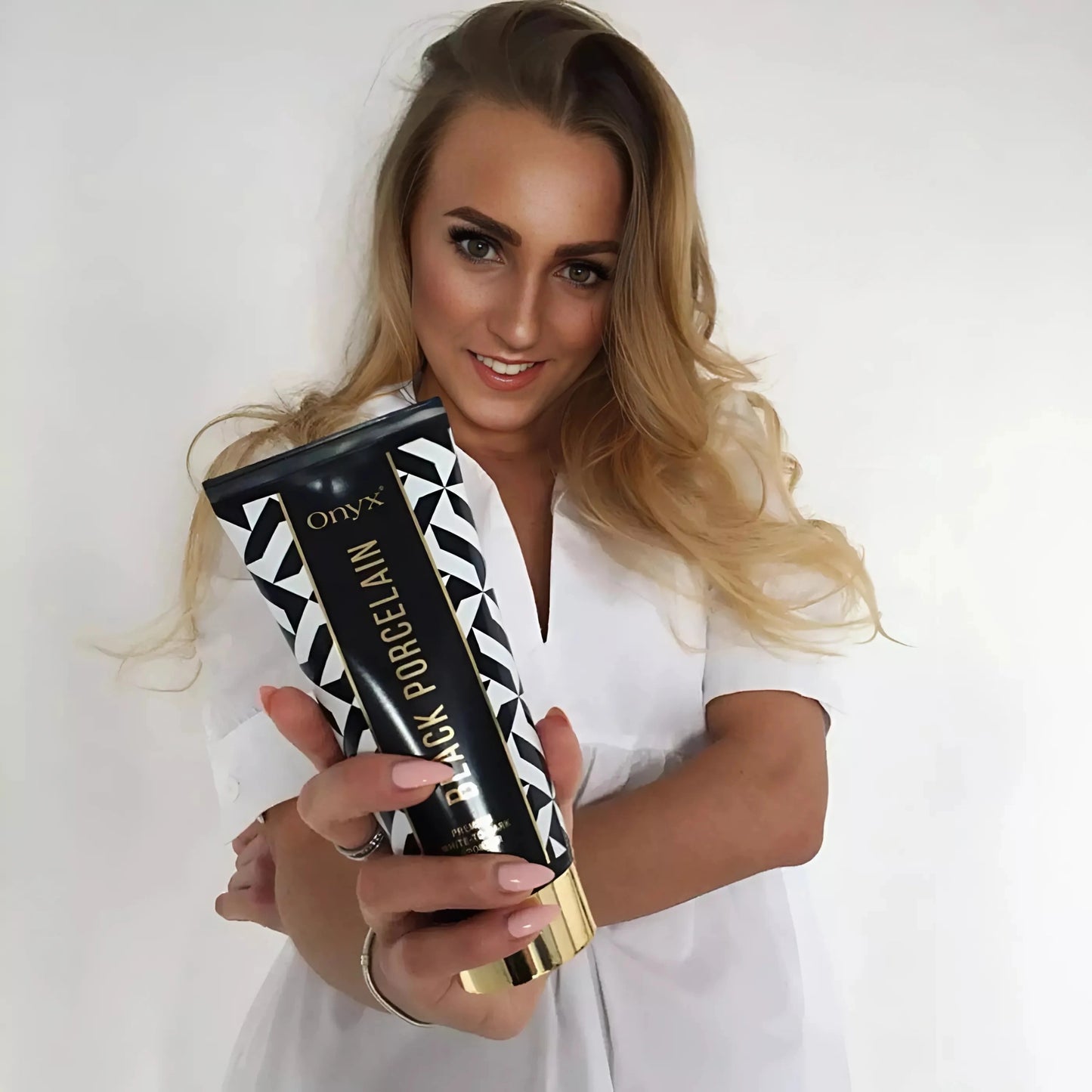 Primer plano de una mujer rubia con la loción bronceadora Onyx Black Porcelain, mostrando el producto con una sonrisa amigable