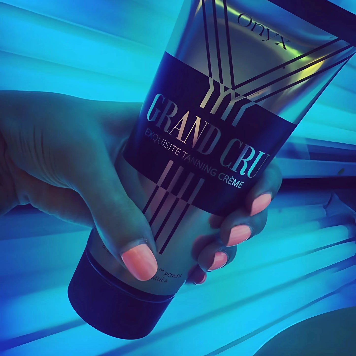 Primer plano de una mano con la Loción Bronceadora Onyx Grand Cru frente a lámparas UV azules en el solarium – fórmula de bronceado intenso
