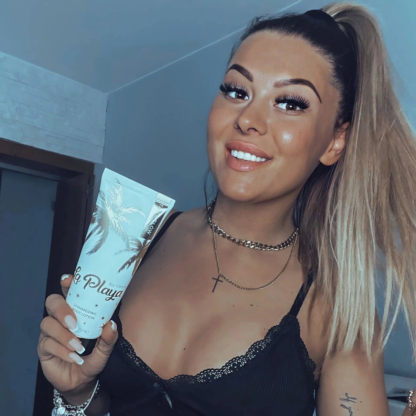 Mujer radiante sostiene la loción corporal Onyx La Playa Glow con piel luminosa