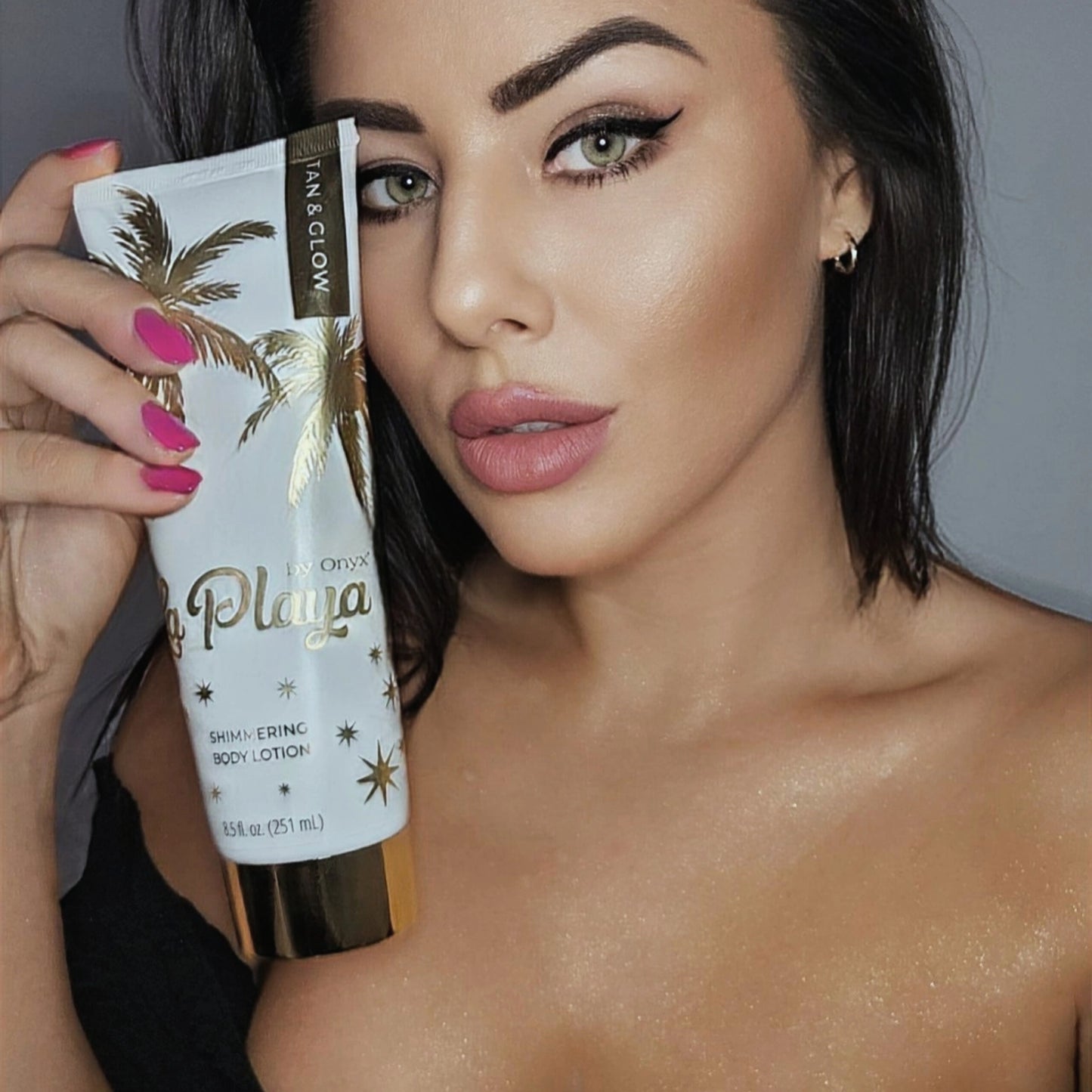 Mujer sostiene la loción corporal Onyx La Playa Glow y muestra piel con destellos en la parte superior del cuerpo