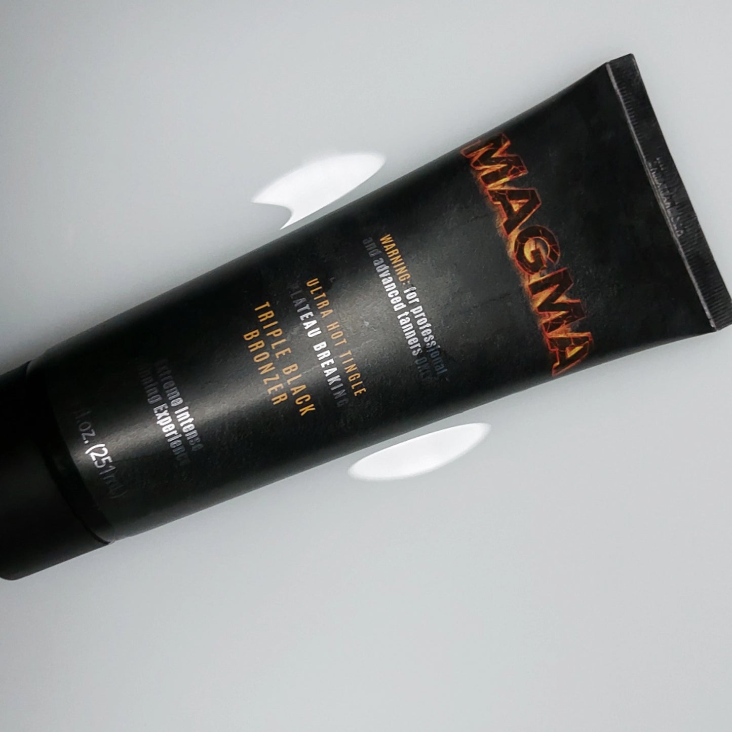 Loción bronceadora Onyx Magma con manchas visibles de crema sobre superficie blanca lisa – tubo en posición lateral con información del producto claramente legible
