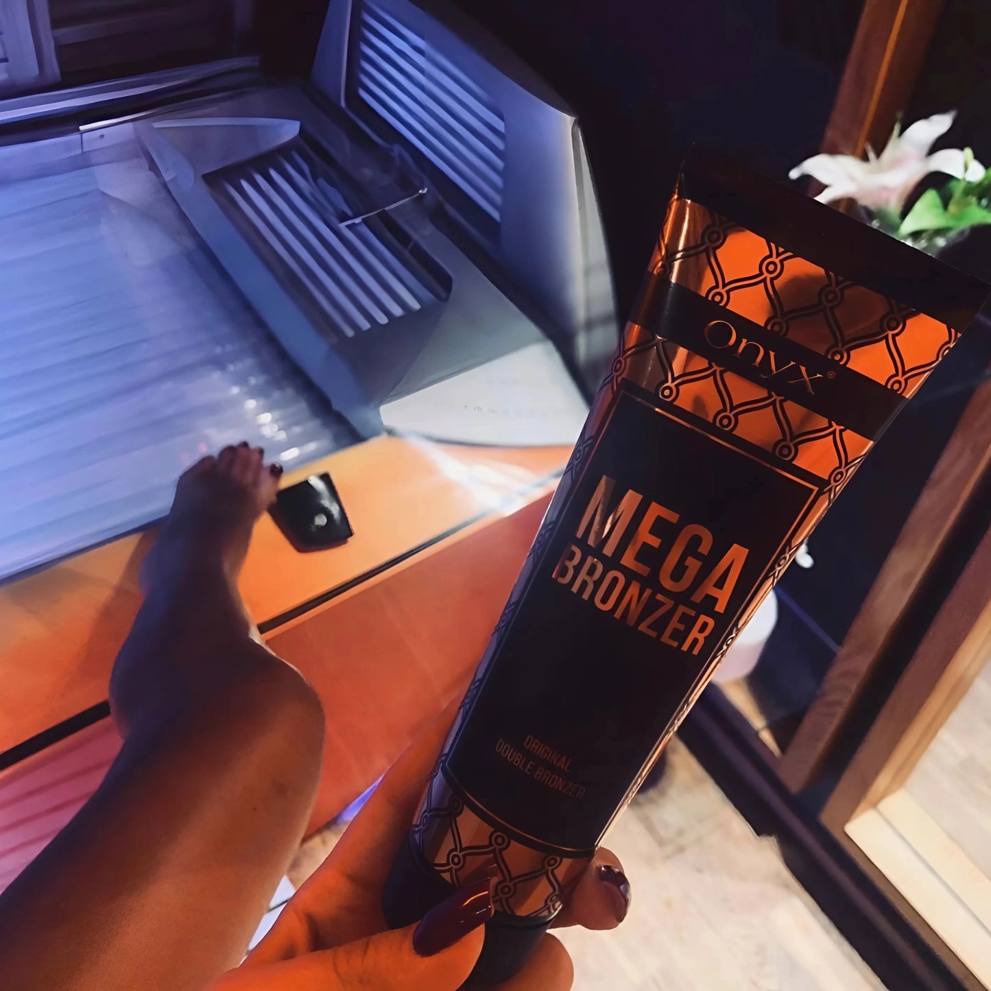Primer plano de una mano con Onyx Mega Bronzer en un solarium iluminado en rojo, preparación perfecta para un bronceado oscuro.