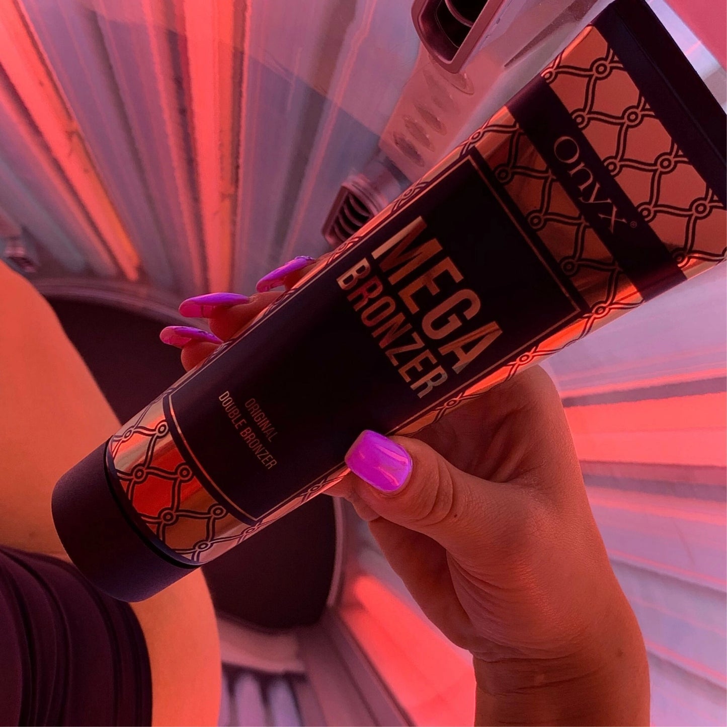 Mano con uñas pintadas de rosa sostiene la loción Mega Bronzer en un solarium con luz roja, mostrando la aplicación en tiempo real.
