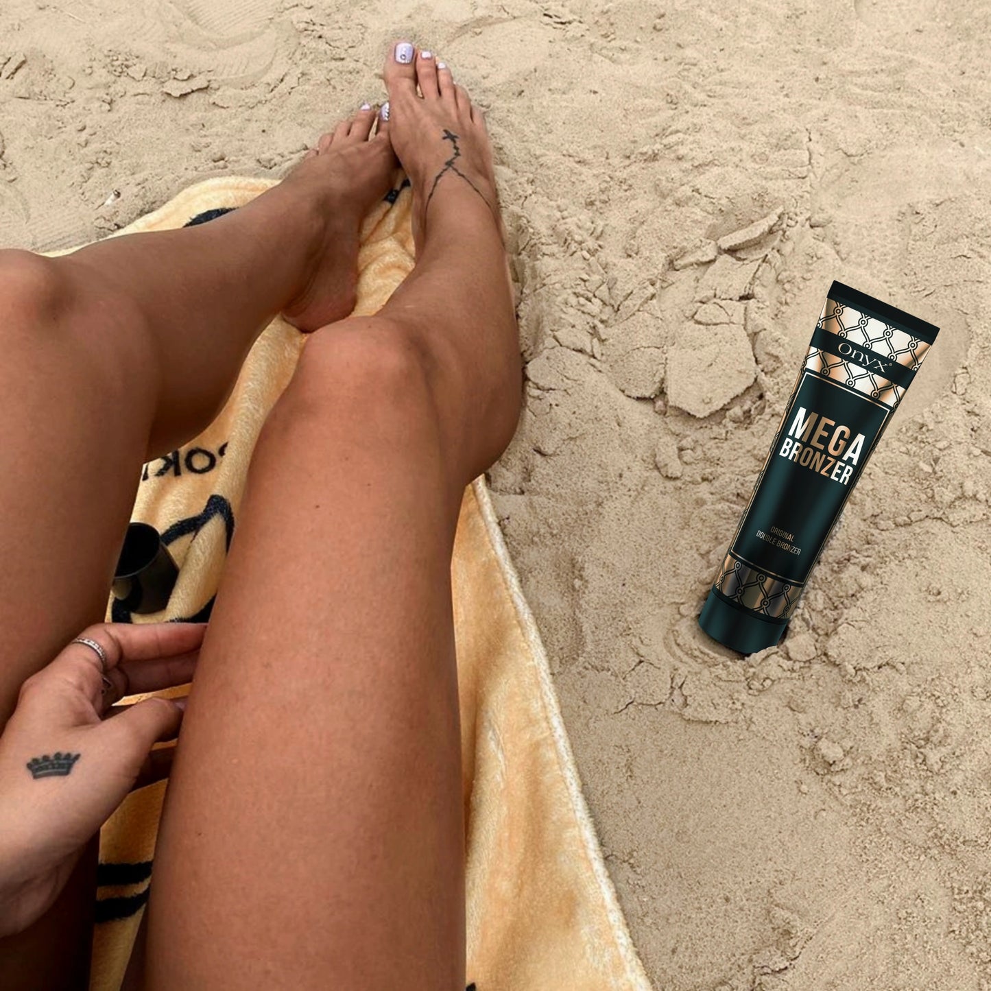 Tubo de Onyx Mega Bronzer sobre la arena junto a unas piernas bronceadas, muestra un bronceado natural tras su uso en la playa.