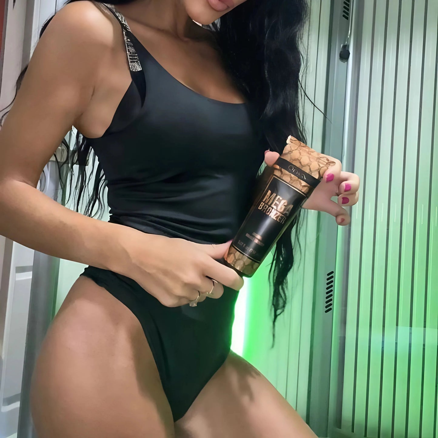 Mujer frente a una cama de bronceado vertical sostiene la loción Mega Bronzer, perfecta para preparar la piel para un bronceado profundo y sin rayas.