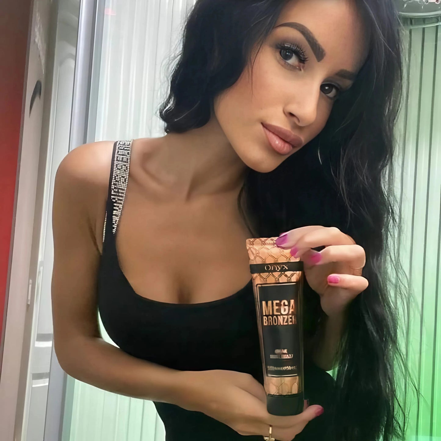 Mujer morena con aire elegante presenta Onyx Mega Bronzer frente a un solarium, ideal para un bronceado profundo y uniforme.
