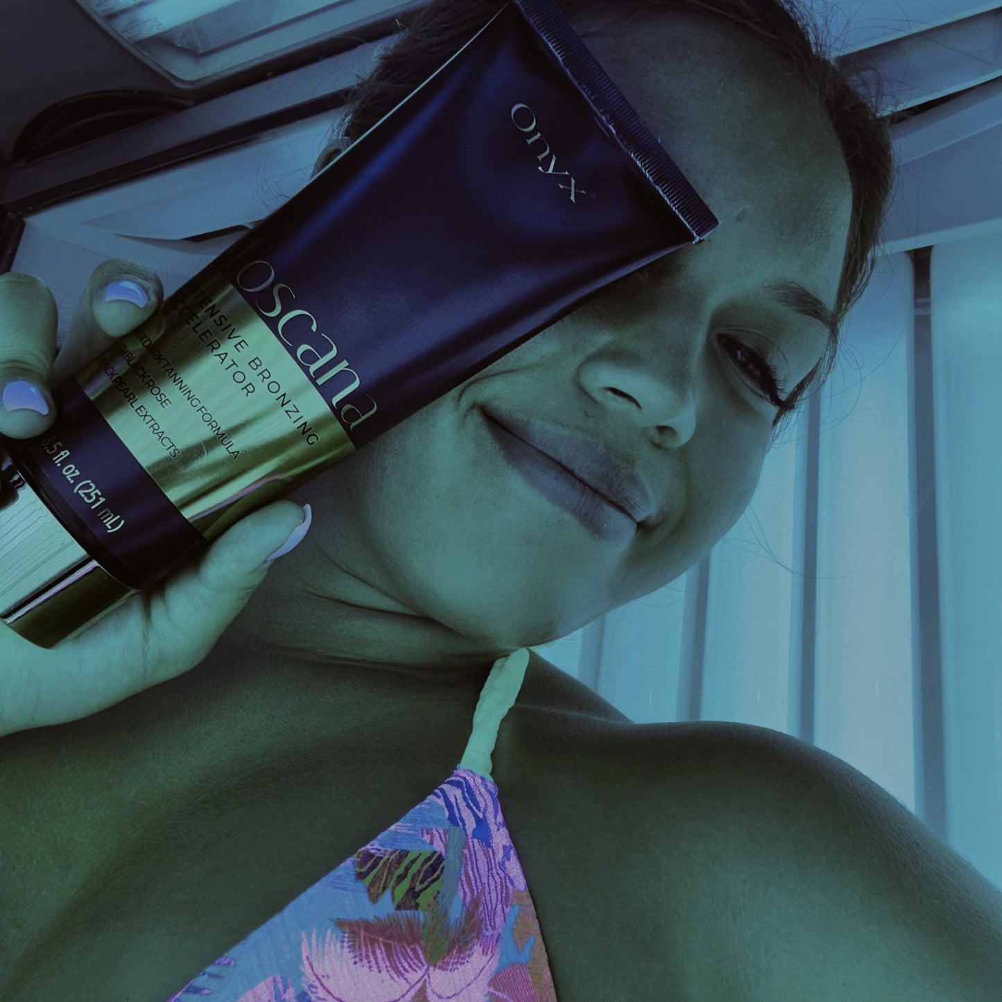 Mujer sonríe y sostiene la loción bronceadora Toscana frente a su rostro en solárium bajo luz azul