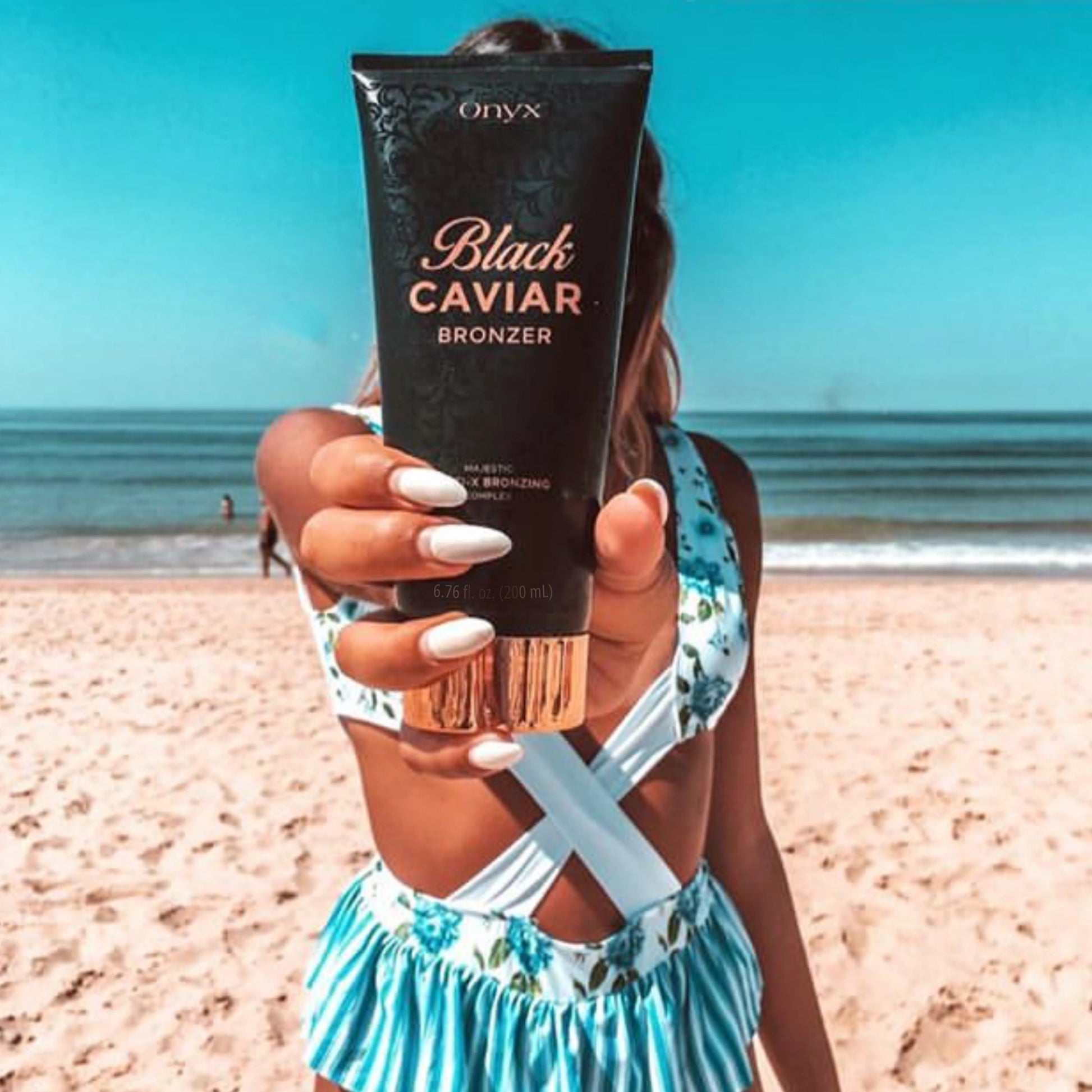 Mujer junto al mar sostiene la loción bronceadora Onyx Black Caviar directamente frente a la cámara, con vista al mar de fondo