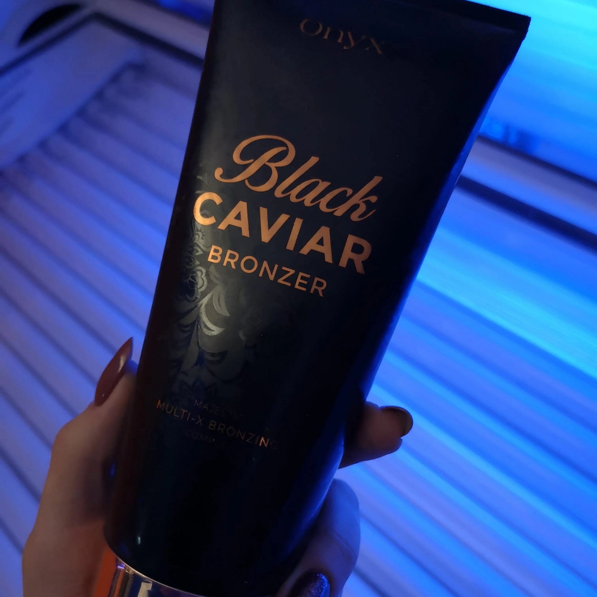 Loción bronceadora Onyx Black Caviar mostrada en primer plano frente a los tubos azules de una cama solar