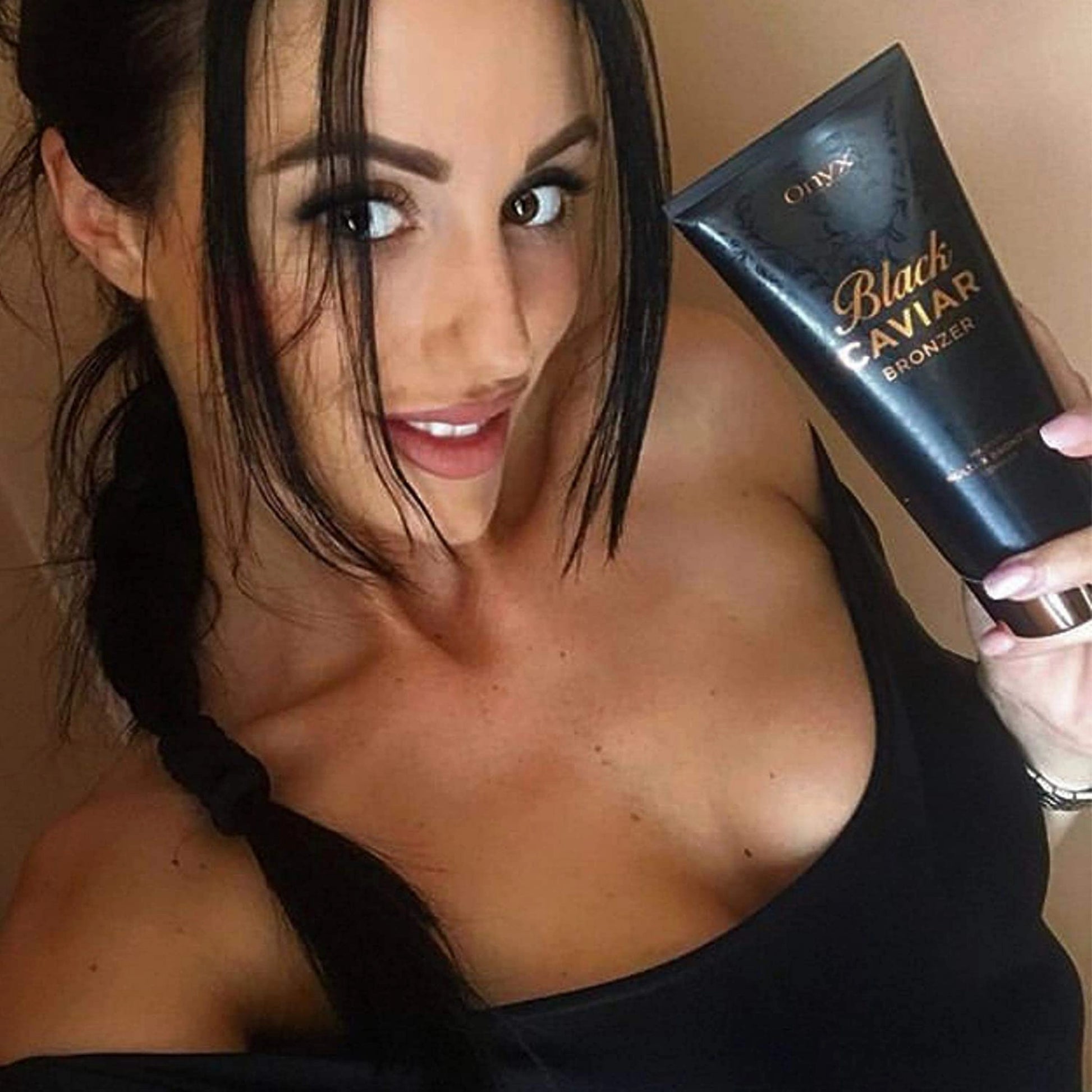 Mujer joven con coleta sostiene la loción bronceadora Onyx Black Caviar y sonríe a la cámara