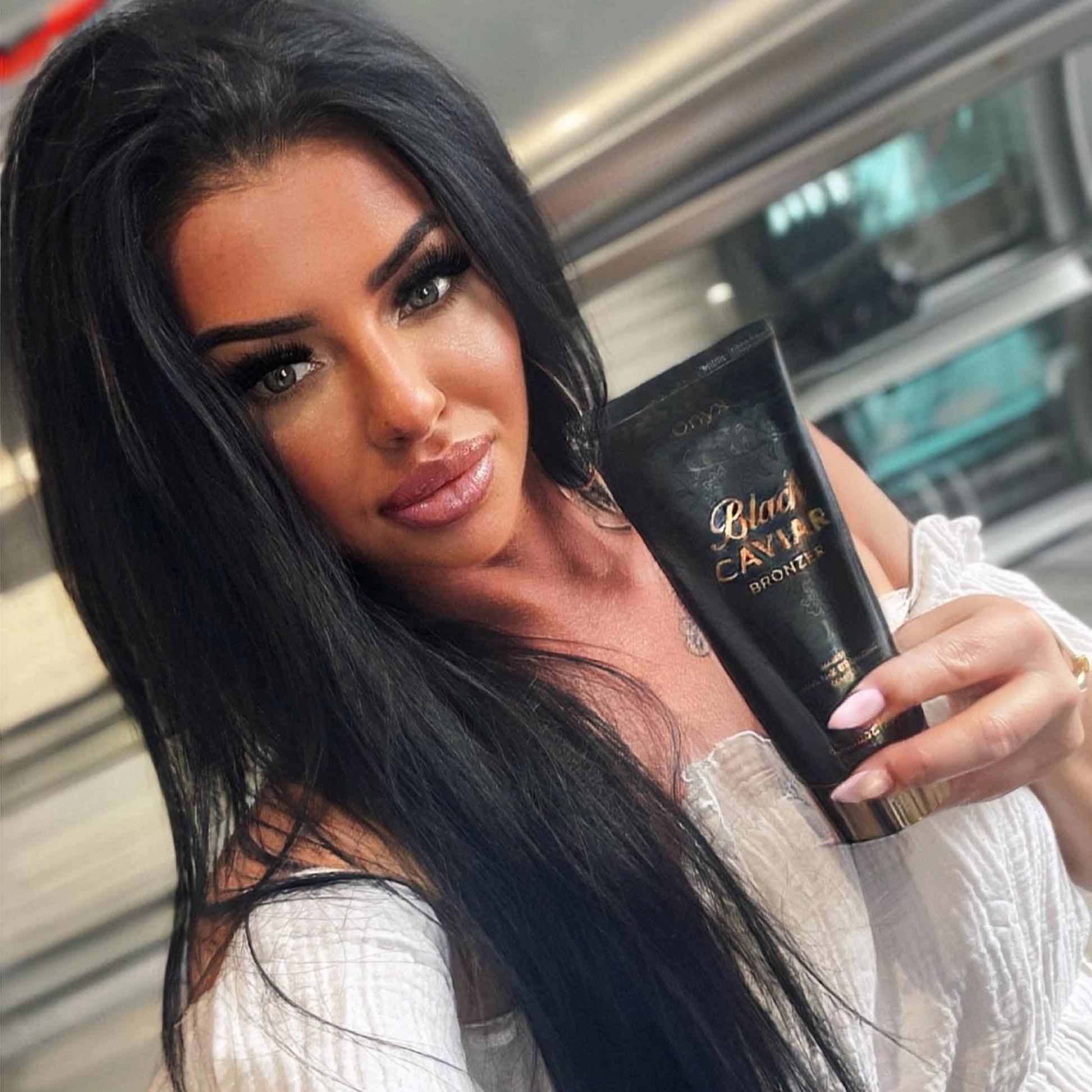 Retrato de una mujer de cabello oscuro con cutis perfecto mostrando la loción bronceadora Onyx Black Caviar
