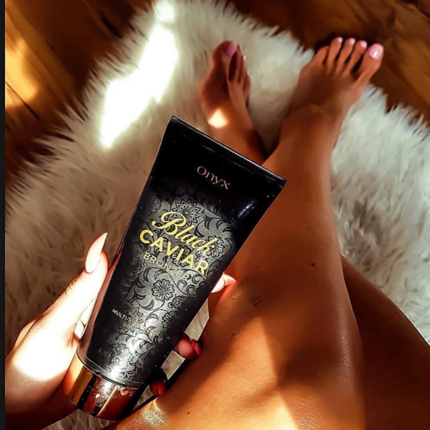 Piernas bronceadas sobre una alfombra blanca sosteniendo la loción bronceadora Onyx Black Caviar