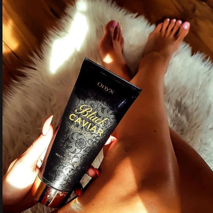 Piernas bronceadas sobre una alfombra blanca sosteniendo la loción bronceadora Onyx Black Caviar