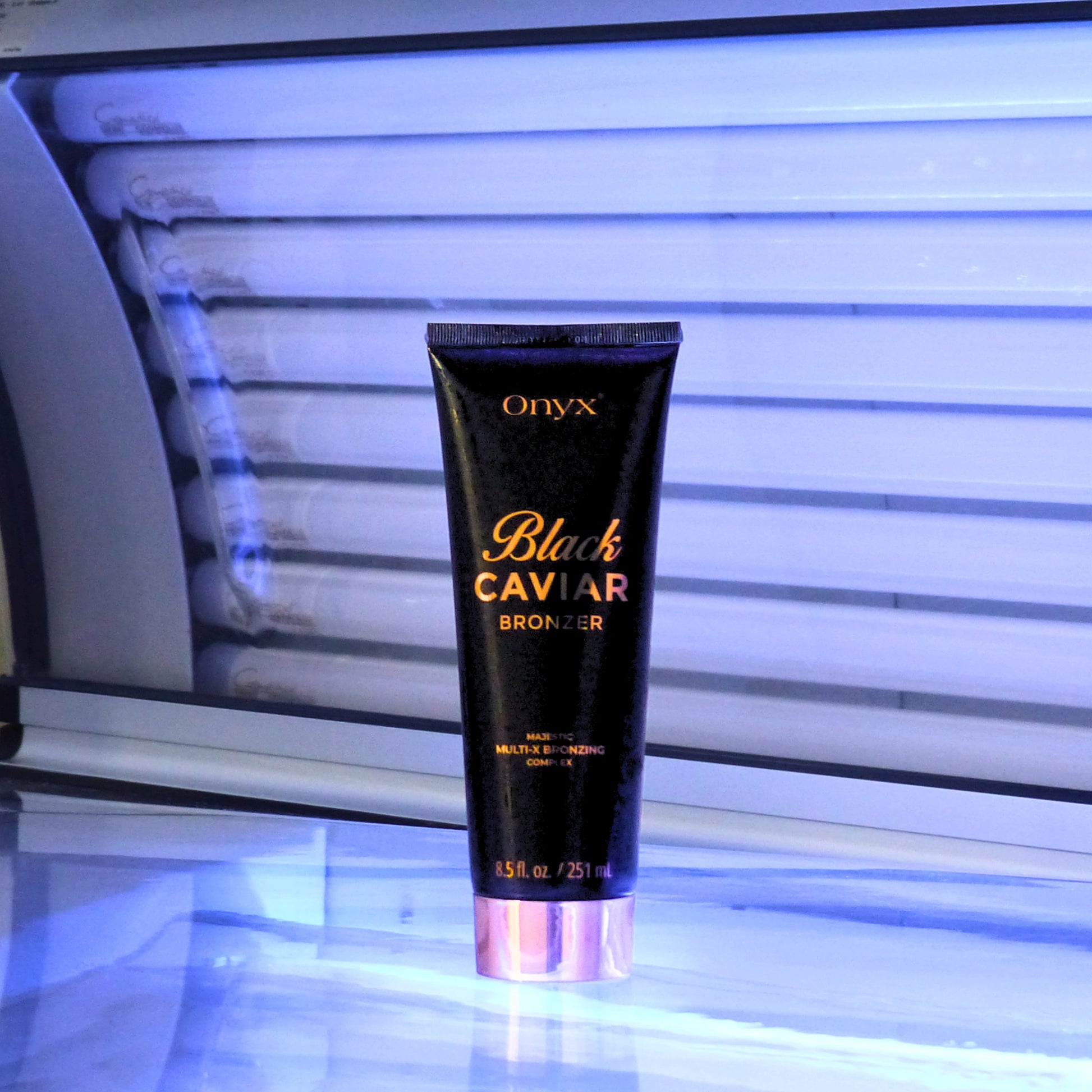 Loción bronceadora Onyx Black Caviar 251 ml frente a una cama solar abierta con iluminación azul y un claro reflejo en la superficie