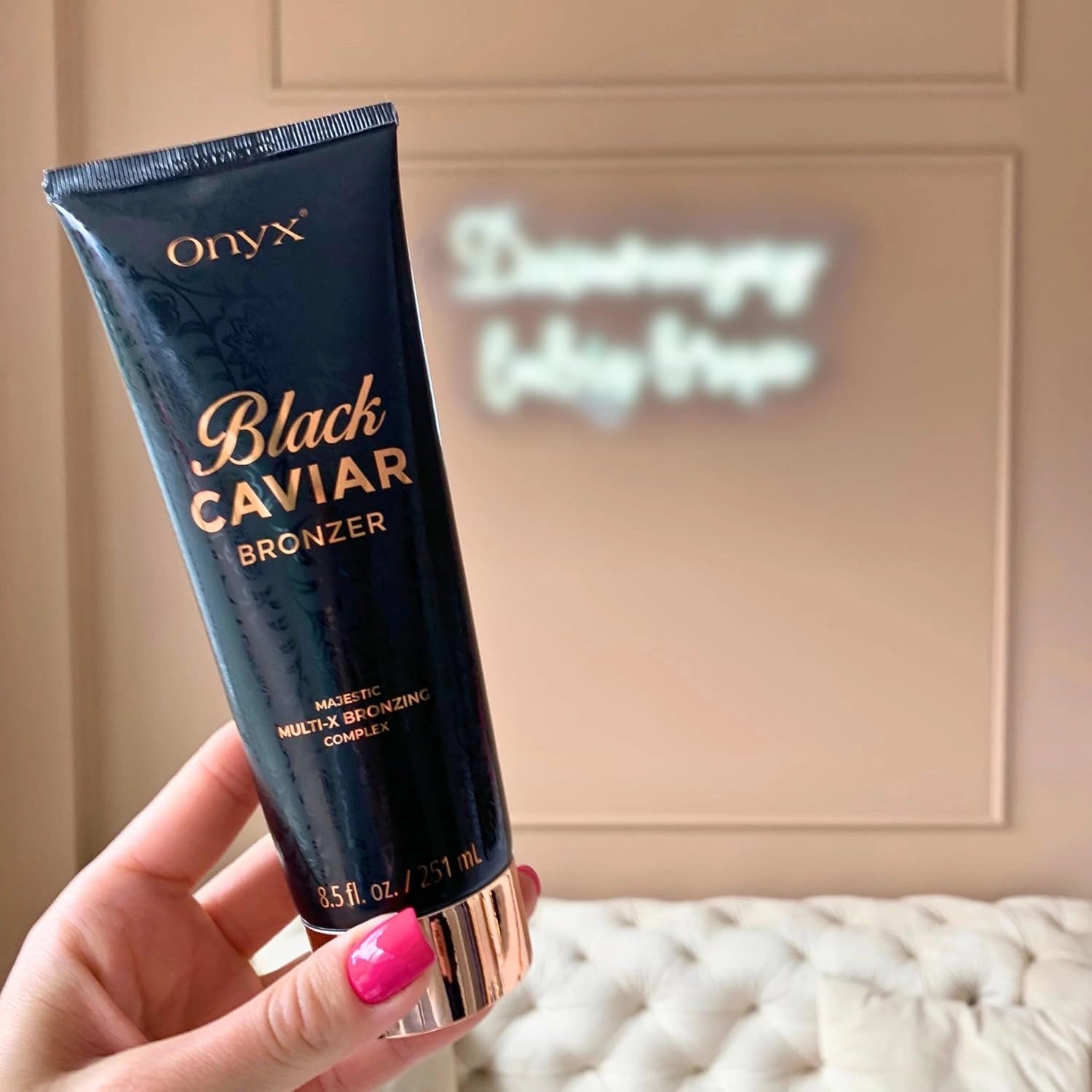 Mujer sostiene la loción Onyx Black Caviar 251 ml frente a una pared color crema y un sofá, con un sutil juego de luces al fondo