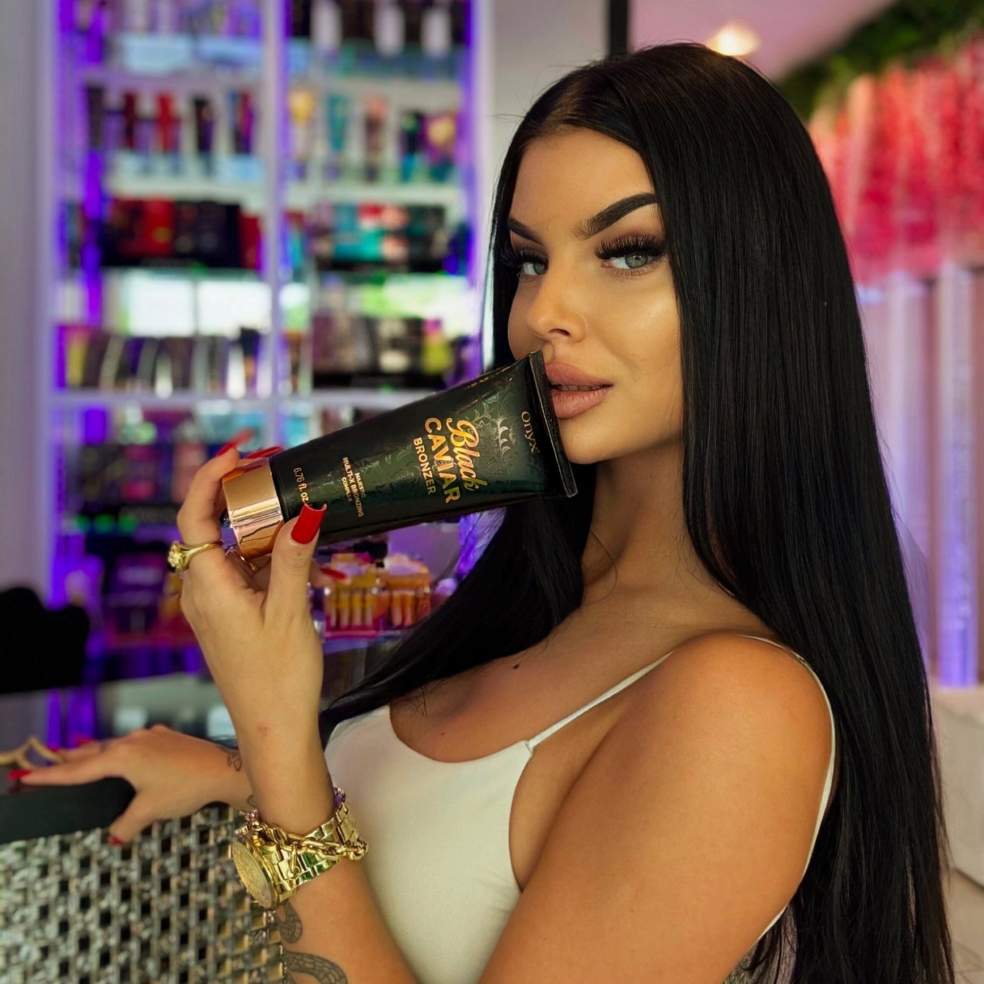 Mujer de cabello largo y oscuro muestra la loción bronceadora Onyx Black Caviar 251 ml en un entorno con productos cosméticos