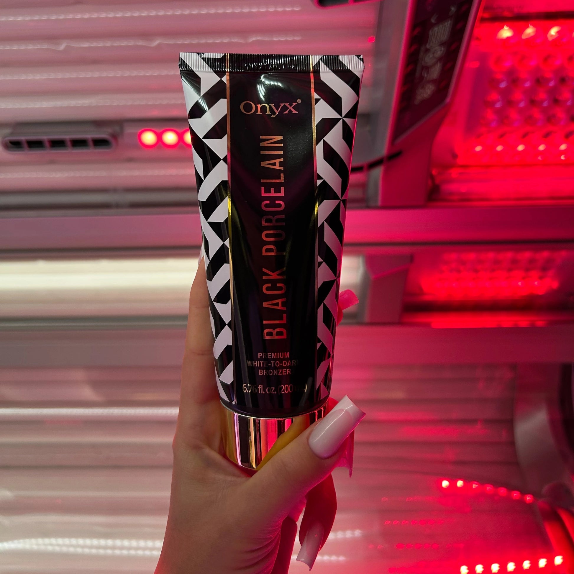 Mano sostiene la loción bronceadora Onyx Black Porcelain frente a intensa luz roja en el solarium, producto ideal para bronceado White-to-Dark