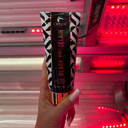 Mano sostiene la loción bronceadora Onyx Black Porcelain frente a intensa luz roja en el solarium, producto ideal para bronceado White-to-Dark