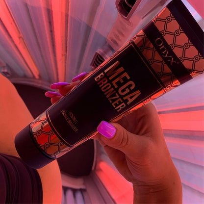 Mano con uñas pintadas de rosa sostiene la loción Mega Bronzer en un solarium con luz roja, mostrando la aplicación en tiempo real.