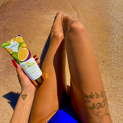 Close-up of tanned legs on the beach with a person holding Onyx Suncolada Accelerator sunbed cream, showing smooth bronzed skin and bright sunlit summer atmosphere.
