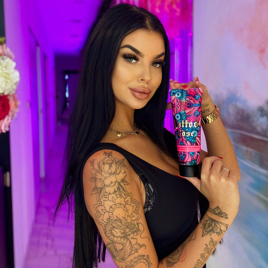 Mujer con cabello largo y tatuaje de dragón en el brazo mostrando la loción bronceadora Onyx Tattoo Rose en una cabina de bronceado con luz violeta